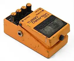 A small effect unit pedal, painted in orange paint that is scuffed from heavy use.